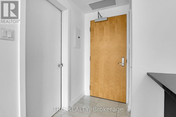 Interior hallway with two doors: one white, one light wood, and tile flooring. - 1110 - 179 Metcalfe Street, Ottawa