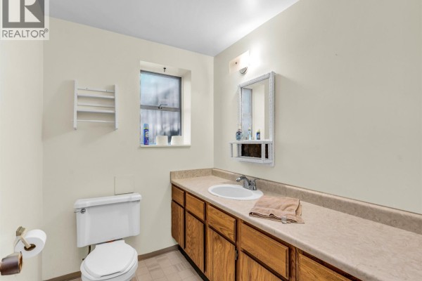 Bathroom with a toilet, vanity with oak cabinets, and a small window. - 1110 Lodge Road, North Vancouver