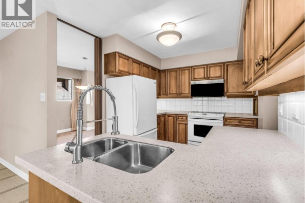 Kitchen with wood cabinets, white appliances, tiled backsplash, and a double sink island. - 1110 Lodge Road, North Vancouver