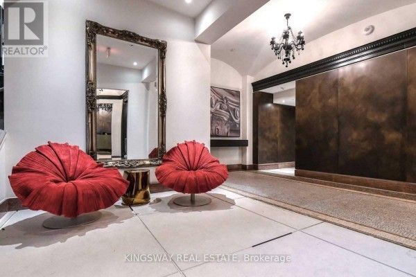 Building lobby with two red sculptural chairs, a large ornate mirror, and dark textured walls. - 1111 - 197 Yonge Street, Toronto