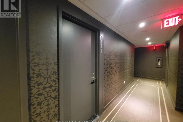 Apartment hallway with patterned dark wallpaper, a grey door labeled '1111', and red exit signs. - 1111 - 197 Yonge Street, Toronto