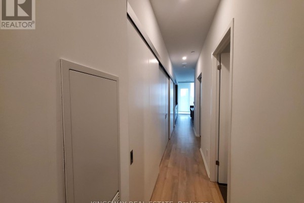 Narrow white hallway with a sliding door on the left and hardwood floors leading to a doorway. - 1111 - 197 Yonge Street, Toronto