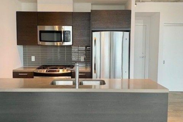 Kitchen with dark wood cabinetry, stainless steel appliances, gas stove, and subway tile backsplash. - 1111 - 318 King Street E, Toronto