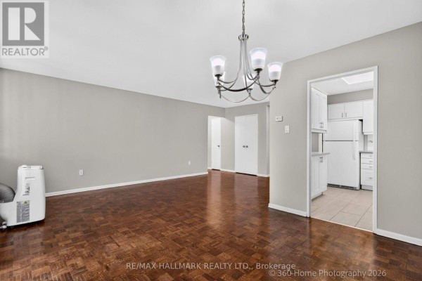 Living and dining area with dark hardwood floors, grey walls, a chandelier, and a view into the kitchen. - 1111 - 360 Ridelle Avenue, Toronto