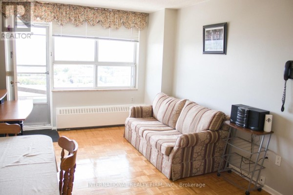 Living room with striped sofa, wooden floor, radiator, and large window. - 1111 - 50 Lotherton Pathway, Toronto