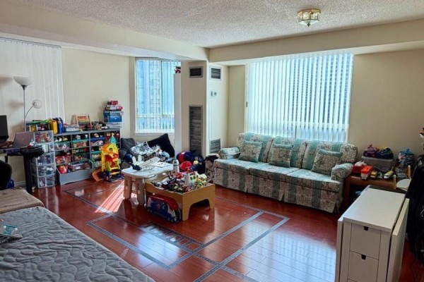 Living room with a floral sofa, coffee table, and floor-to-ceiling windows with vertical blinds. - 1111 - 633 Bay Street, Toronto