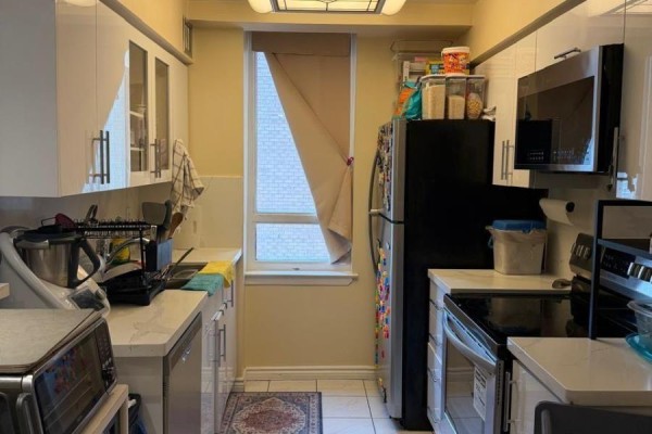 Narrow galley kitchen with white cabinets, stainless steel appliances, and a window with beige curtains. - 1111 - 633 Bay Street, Toronto