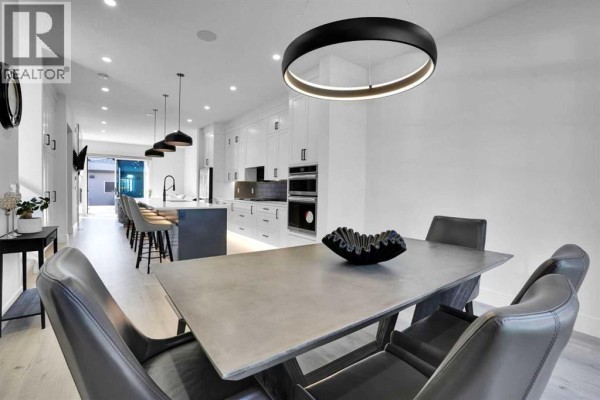 Open-concept dining and kitchen area with concrete table, modern kitchen, and island with stools. - 1111 43 Street Sw, Calgary