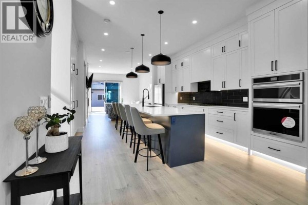 Modern kitchen with white cabinets, dark backsplash, large island with bar stools, and pendant lights. - 1111 43 Street Sw, Calgary