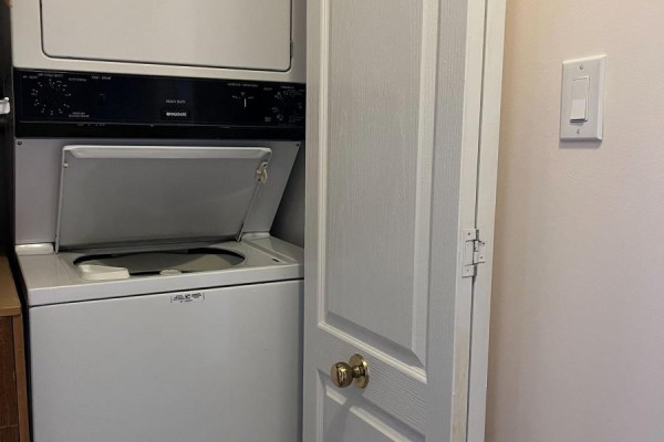 Stacked white washing machine and dryer inside a closet with a white door and brass knob. - 1112 - 1883 Mcnicoll Avenue, Toronto