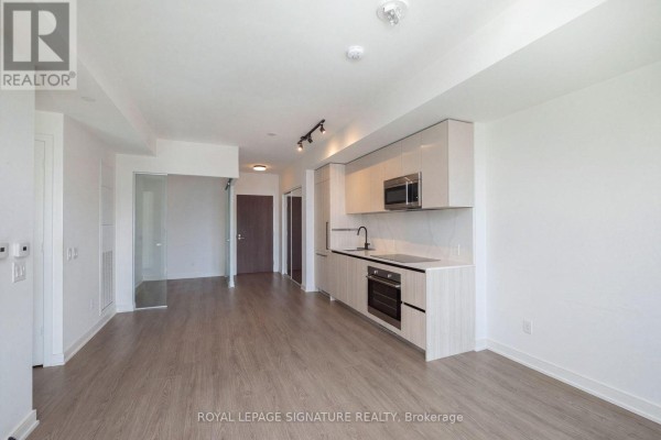 Open concept kitchen with light wood cabinetry, black countertops, and stainless steel appliances, overlooking living area. - 1112 - 425 Front Street E, Toronto