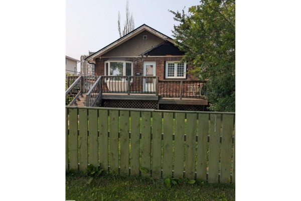 Wooden fence in front of a brick house with a deck and entranceway. - 11124 97 St Nw Nw, Edmonton