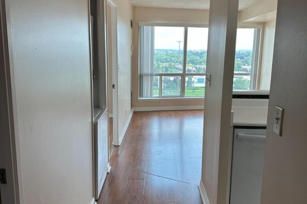 View from an apartment hallway showing a living area with a large window and wooden floor. - 1113 - 18 Lee Centre Drive, Toronto