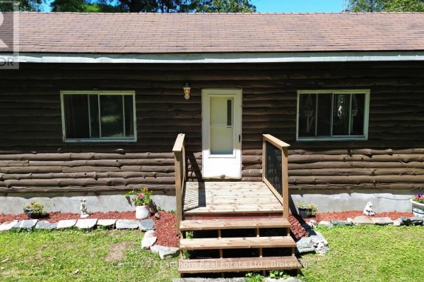 Close-up of the log-style house front entrance with a wooden deck and railing. - 1113 Clark Road, Frontenac