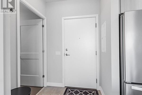 Apartment entrance hallway with a white door, light grey walls, and wood laminate flooring. - 1114 - 7895 Jane Street, Vaughan