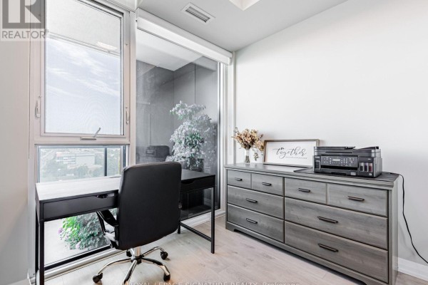 Home office with a black metal desk and chair, grey dresser, and large window overlooking the city. - 1114 - 7895 Jane Street, Vaughan