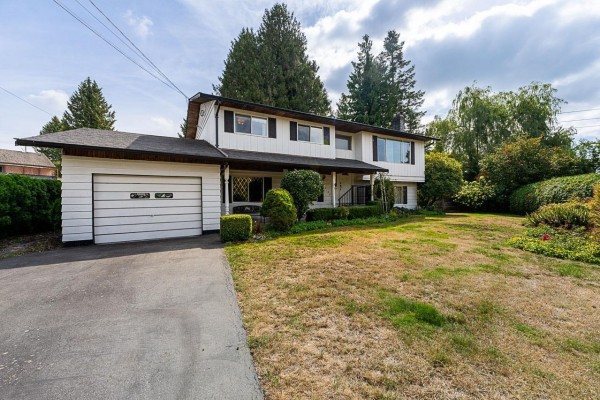 Side exterior view of a white two-story house with a sloped roof and mature trees. - 11142 Patricia Drive Drive, Delta
