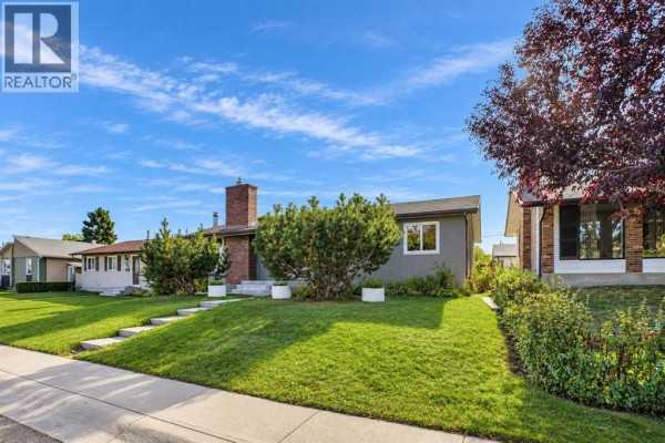 Side view of a grey bungalow with a well-maintained lawn and landscaped bushes. - 1115 Marcombe Crescent Ne, Calgary