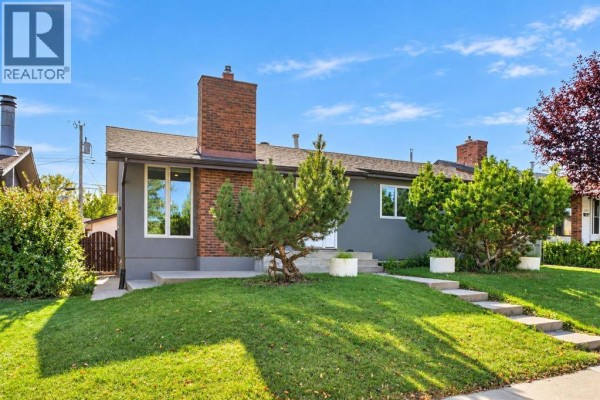 Front view of a grey bungalow with a large brick chimney and large windows. - 1115 Marcombe Crescent Ne, Calgary