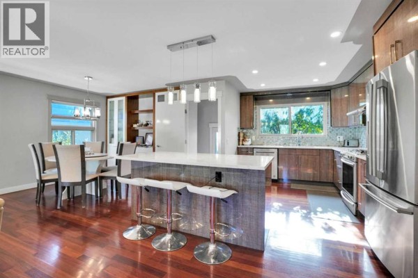 Kitchen and dining area with a large island, pendant lights, stainless steel appliances, and wood cabinets. - 1115 Marcombe Crescent Ne, Calgary