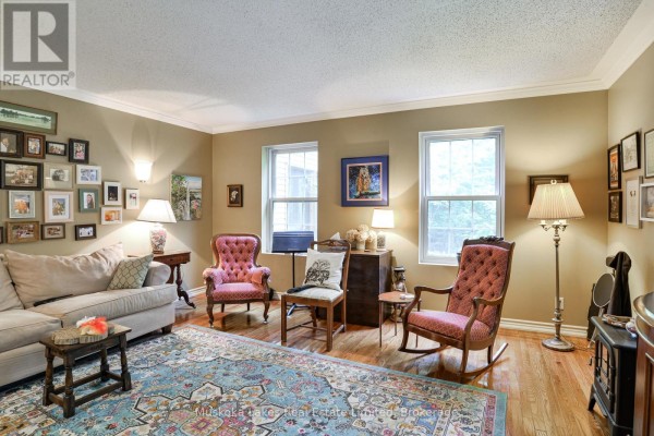 Living room with two tufted armchairs, a sofa, a patterned rug, and two windows overlooking greenery. - 1115 Partridge Lane, Bracebridge)
