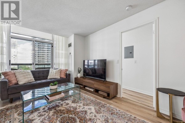 View of living room, television, and doorway leading to bedroom with a bed. - 1116 - 503 Beecroft Road, Toronto