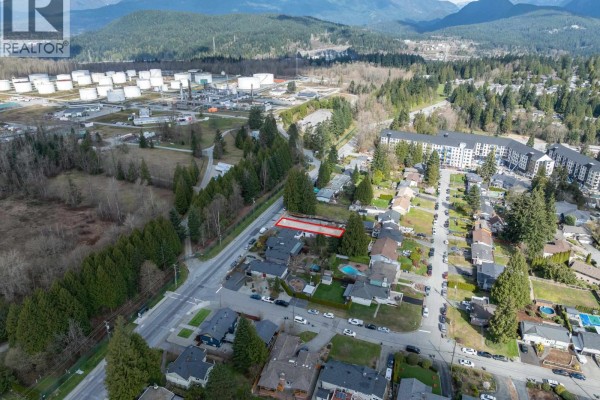 Aerial view of residential area showing the lot for sale near industrial buildings and mountainous backdrop. - 1116 Glenayre Drive, Port Moody