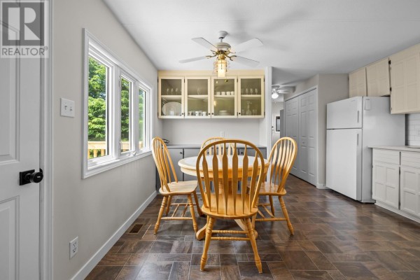 Kitchen and dining area showing a white refrigerator, cabinets, and a round wooden table with four chairs. - 1116 St. Charles Road, Souris West