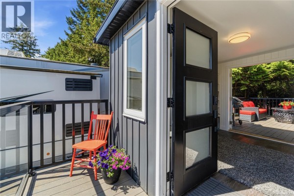 Entrance to the mobile home with a black door and an orange chair on the deck. - 1116 Woss Lake Dr, Nanaimo