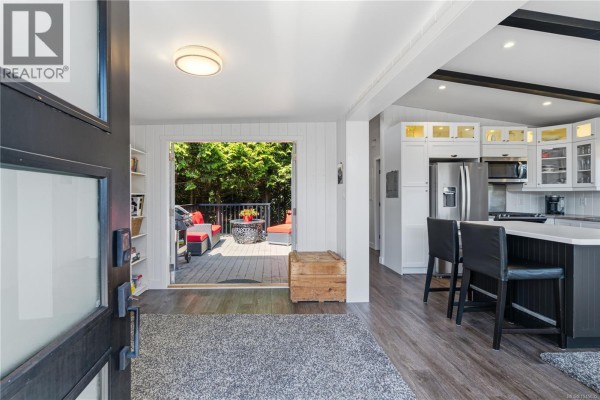 Interior view of the mobile home showing the kitchen, island, and deck access. - 1116 Woss Lake Dr, Nanaimo
