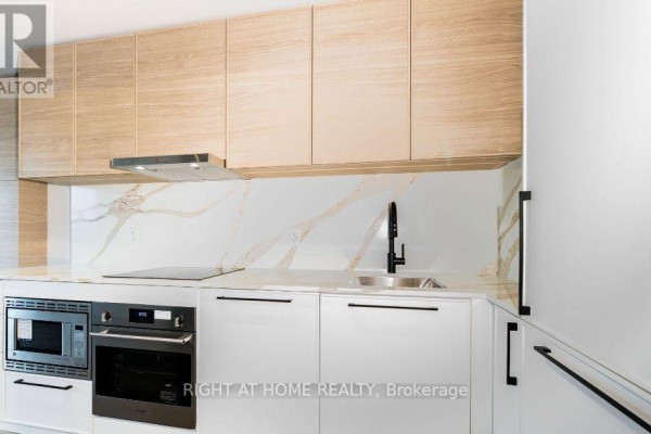 Corner view of a contemporary kitchen with light wood upper cabinets and white lower cabinets. - 1117 - 1050 Eastern Avenue, Toronto