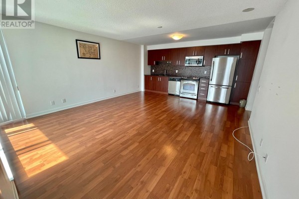 Open concept living area with wood floors and view of galley kitchen with dark wood cabinets and stainless steel appliances. - 1117 - 17 Anndale Drive, Toronto