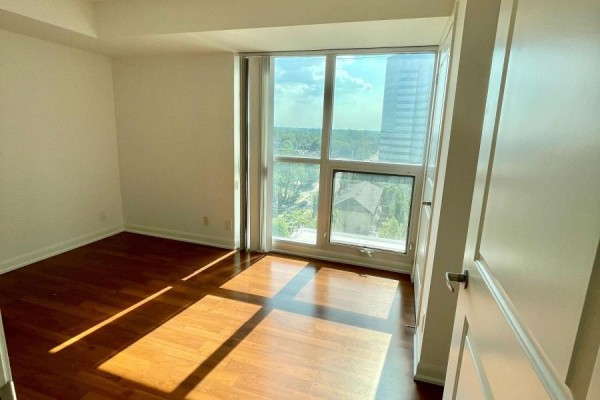 Bedroom with large window showing city view, wood floors, and white walls. - 1117 - 17 Anndale Drive, Toronto