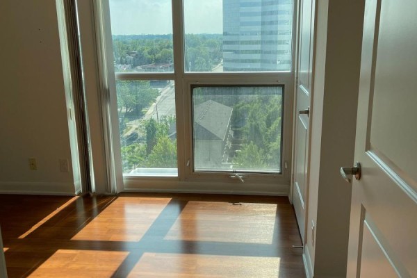 View through bedroom window with sunlight streaming onto wood floors and city buildings outside. - 1117 - 17 Anndale Drive, Toronto