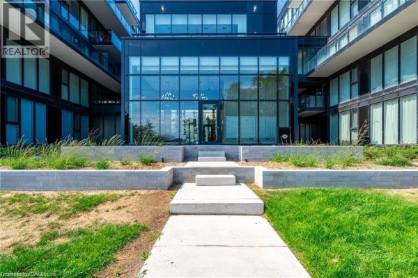 Pathway leading to the glass-fronted entrance of a contemporary apartment building with manicured landscaping. - 1117 Cooke Boulevard Unit# A305, Burlington