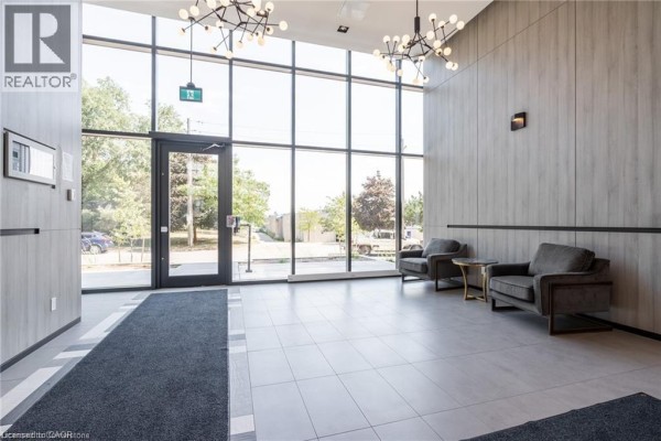Building lobby with large windows, two grey armchairs, a small table, and a dark grey rug. - 1117 Cooke Boulevard Unit# A305, Burlington