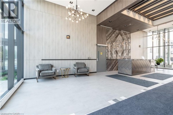 Apartment building lobby featuring a reception desk, two armchairs, and modern light fixtures. - 1117 Cooke Boulevard Unit# A305, Burlington