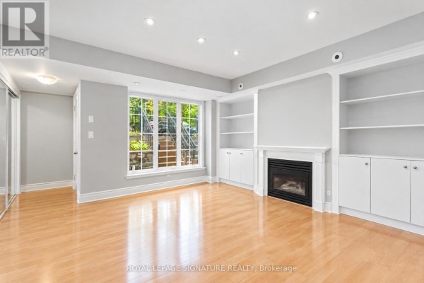 Living room with fireplace, built-in shelves, and window with a view of stairs and trees. - 1119 - 5 Everson Drive W, Toronto