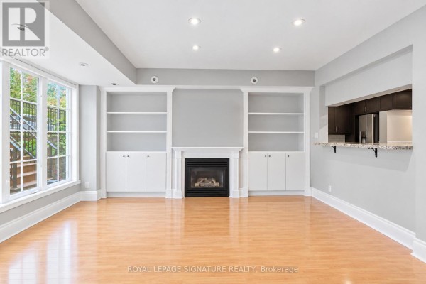 Living room with fireplace, built-in shelving, and view into kitchen area with bar seating. - 1119 - 5 Everson Drive W, Toronto
