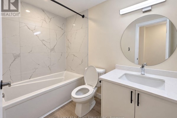 Bathroom with a white tub, toilet, and vanity with a round mirror above the sink. - 1119 Heron Road, Ottawa