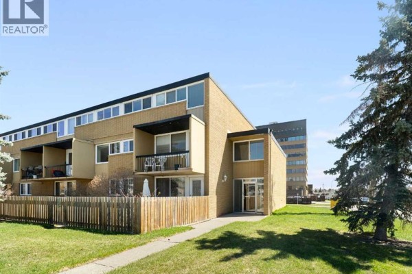 Side exterior view of a brick apartment building with balconies and a concrete walkway. - 112, 7007 4a Street Sw, Calgary