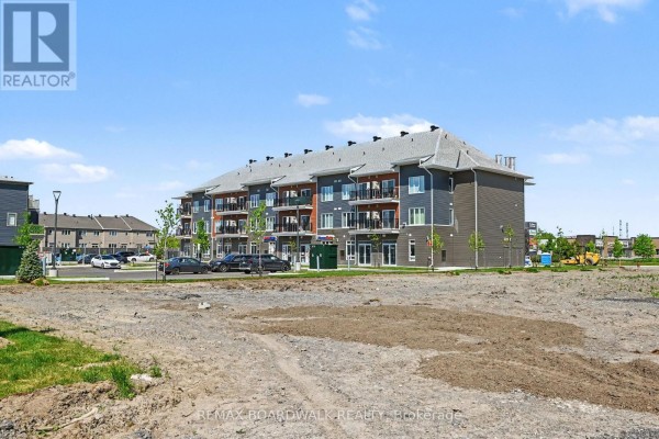 View of a modern apartment building with balconies, dark grey siding, and surrounding undeveloped land. - 112 - 2370 Tenth Line Road, Ottawa