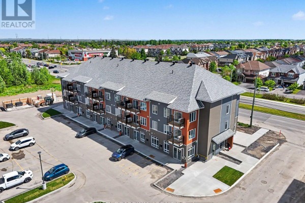 Aerial view of a three-story apartment building with a grey roof, balconies, and a parking lot in front. - 112 - 2370 Tenth Line Road, Ottawa