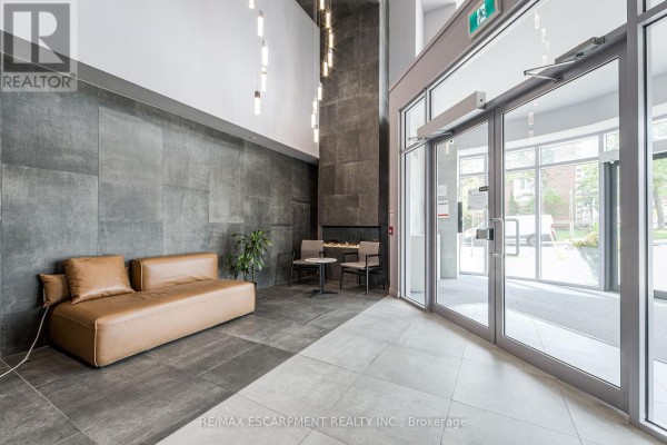 Building lobby with a brown leather sofa, two chairs, a modern fireplace, and grey tiled walls. - 112 - 2433 Dufferin Street, Toronto