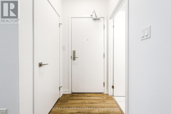 Bright white hallway with three doors, wooden flooring, and light switches. - 112 - 2433 Dufferin Street, Toronto