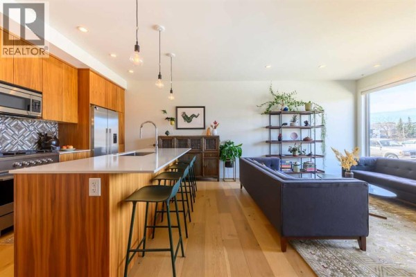 Kitchen island with stools, stainless steel appliances, and adjacent living room. - 112 21 Street Nw, Calgary
