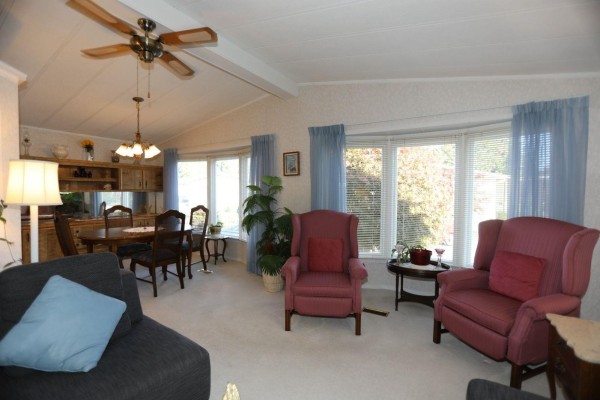 Dining area with a wooden table and chairs next to a bay window with red armchairs. - 112 2303 Cranley Drive, Surrey