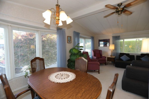 View from the dining area shows a wooden table and chairs, bay windows, and living room furniture. - 112 2303 Cranley Drive, Surrey