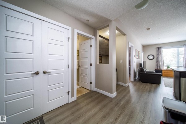 Apartment hallway with white doors, wood-look flooring, leading to living areas. - #112 2588 Anderson Wy Sw, Edmonton