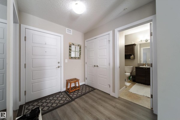 Apartment entryway with white doors, wood-look flooring, and bathroom visible. - #112 2588 Anderson Wy Sw, Edmonton